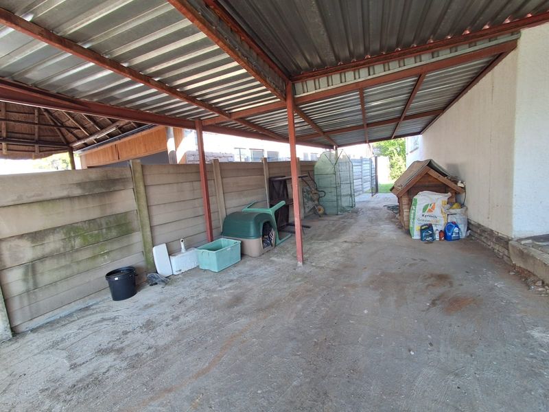 A covered outdoor carport or utility area featuring a corrugated metal roof, steel support structure, and concrete flooring, suitable for vehicle storage.