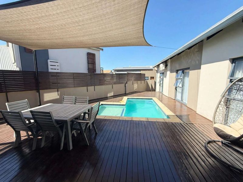 Outdoor entertainment area featuring a swimming pool, timber decking, and a shade sail, providing a private space for relaxation and leisure.