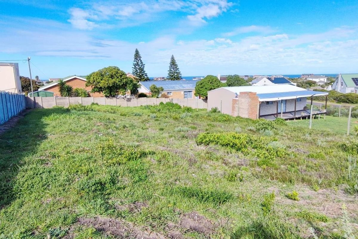 A vacant residential plot featuring a perimeter boundary wall and views of the surrounding neighborhood and distant coastline.
