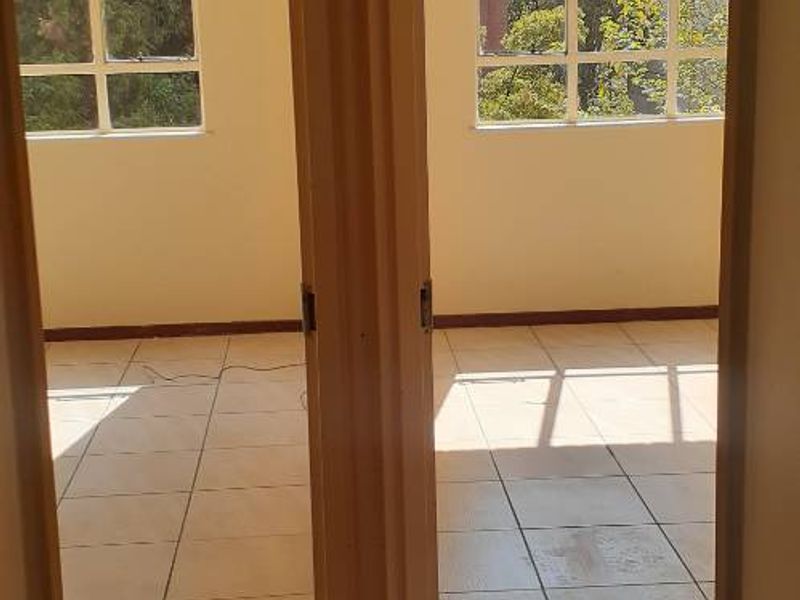 A vacant hallway featuring tiled flooring and dual access points to adjacent rooms with large windows providing natural light.