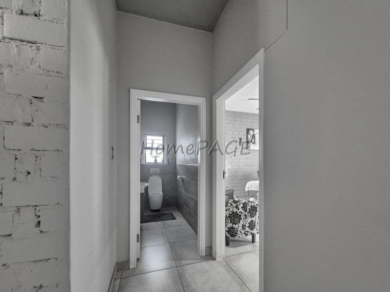 A hallway providing access to a bathroom and bedroom, featuring tiled flooring and an exposed brick wall finish.