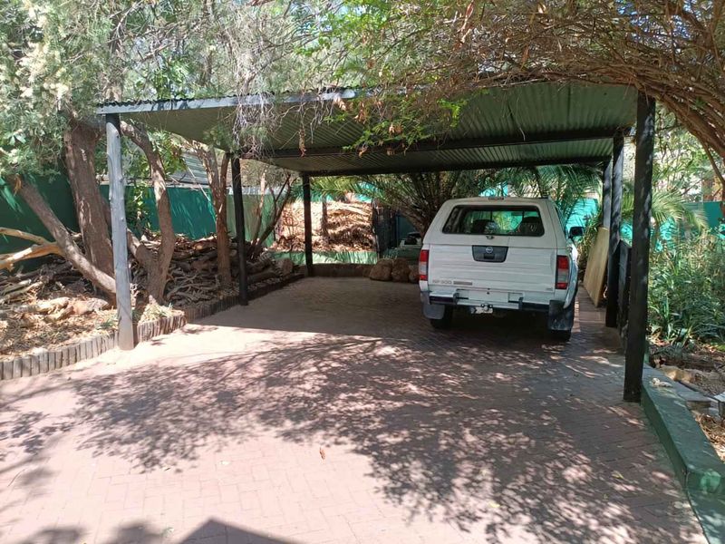A covered outdoor carport area featuring a corrugated metal roof supported by steel posts and paved flooring.