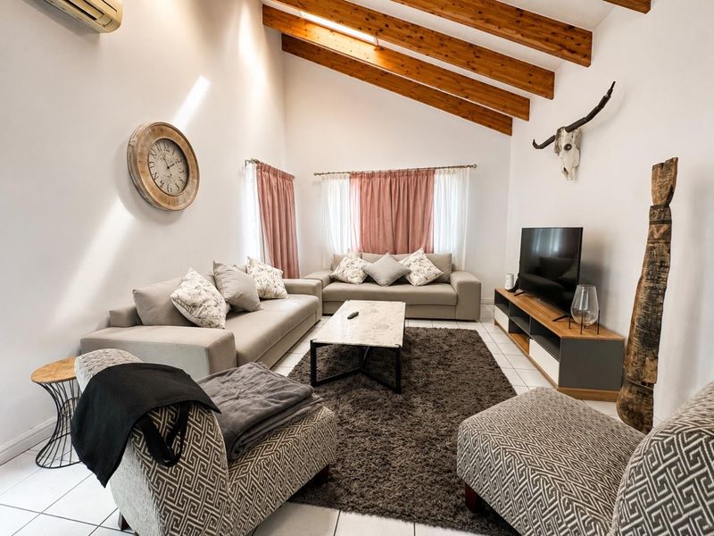 Spacious living room featuring high vaulted ceilings with exposed timber beams, tiled flooring, and a wall-mounted air conditioning unit.
