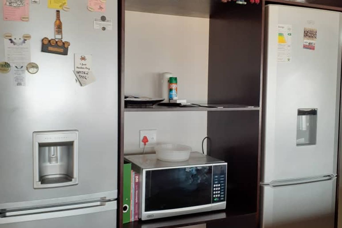 A kitchen storage unit featuring built-in shelving with space for a microwave, flanked by two stainless steel refrigerator units.