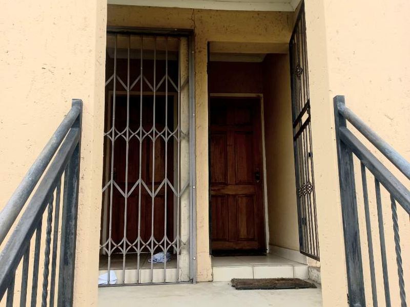 Entrance area of the apartment featuring a concrete staircase, metal handrails, and a secure wooden front door with a metal security gate.