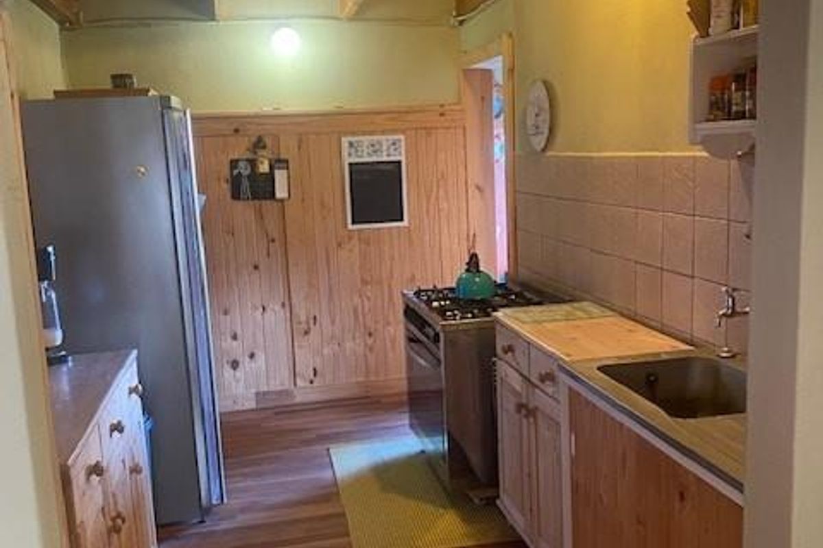 A functional kitchen featuring timber cabinetry, a built-in stove, and a stainless steel sink, characterized by a rustic wood-paneled aesthetic.