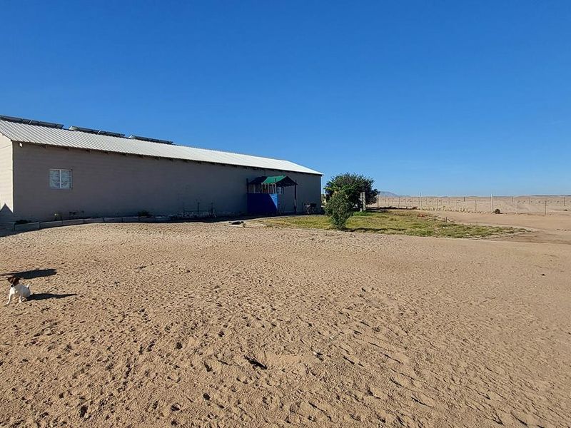 Rear view of the property showing the main building structure with a metal roof and solar panels, set within a large sandy yard.
