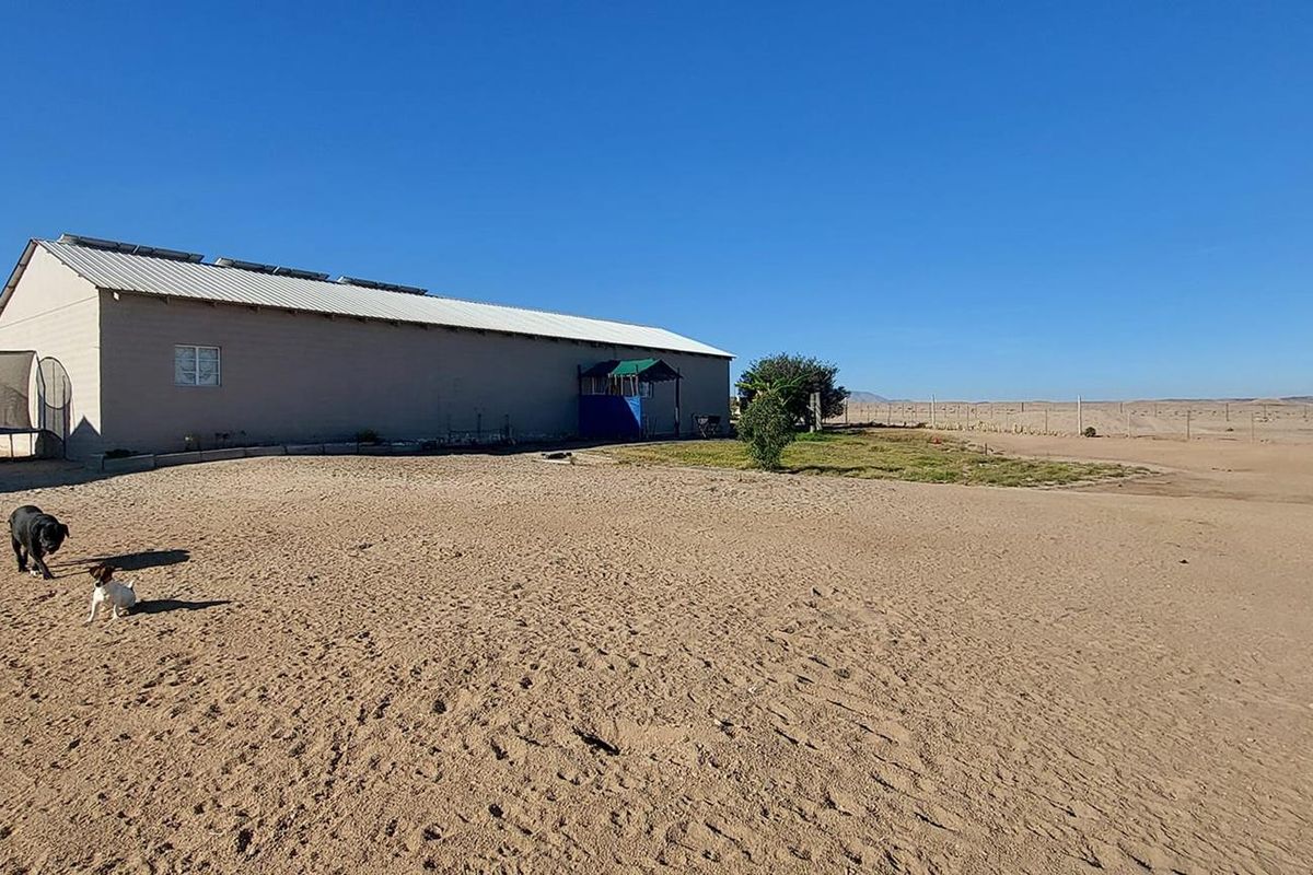 Rear view of the property showing the main building structure with a metal roof and solar panels, set within a large sandy yard.