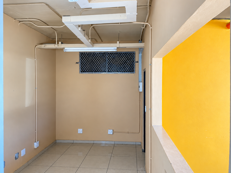 An empty utility or storage space featuring ceramic tiled flooring, exposed electrical and ventilation infrastructure, and a security-grille window.