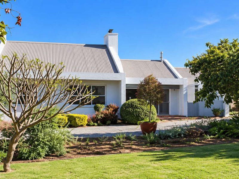 A well-maintained cluster home featuring a clean white facade, corrugated metal roof, and a neatly landscaped front garden with a gravel driveway.