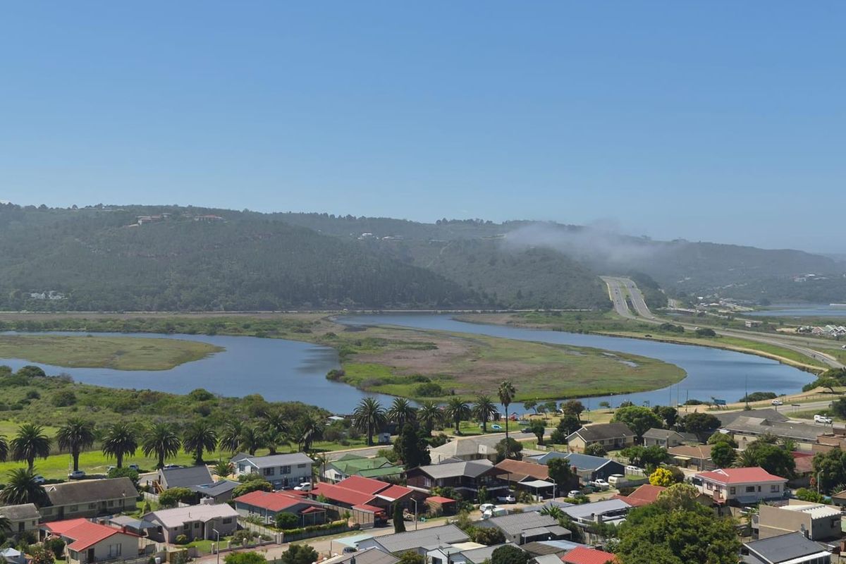 Elevated aerial view overlooking a residential neighborhood, winding river, and distant hills under a clear blue sky.
