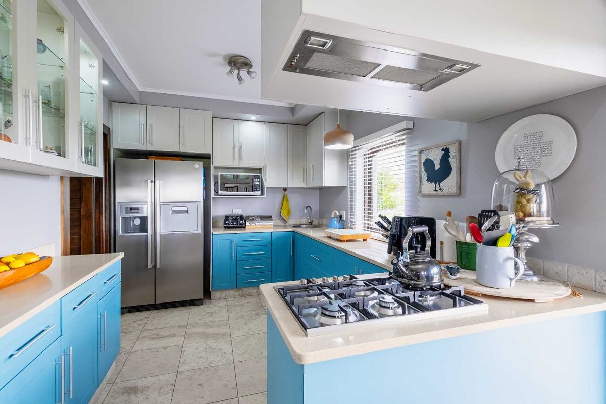 A functional kitchen featuring blue and white cabinetry, stone countertops, a built-in gas hob, stainless steel extractor fan, and tiled flooring.