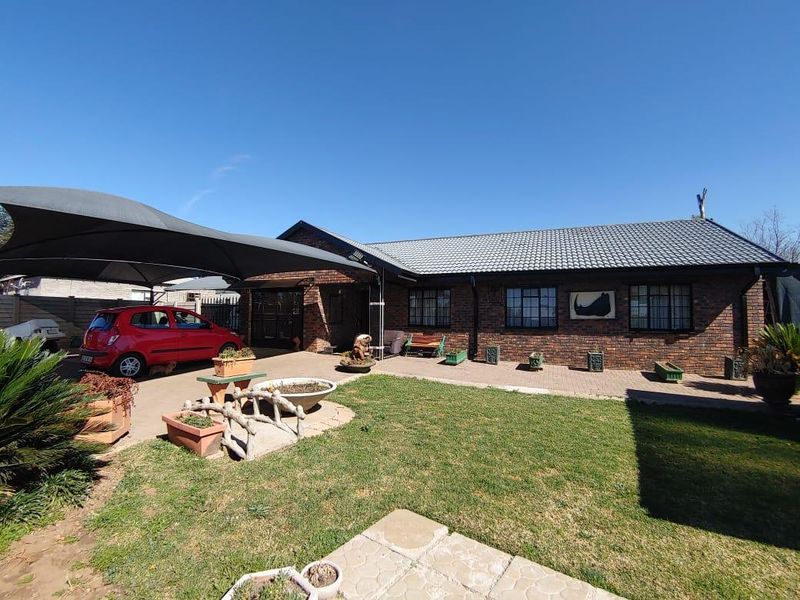 Front exterior view of a brick house featuring a tiled roof, paved driveway, and a large shade sail carport.