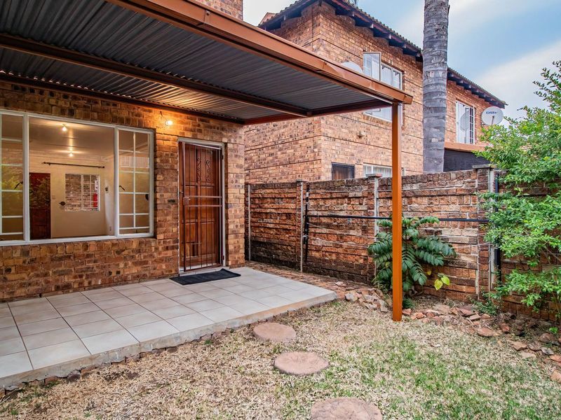 A covered patio area with tiled flooring, featuring a brick boundary wall and direct access to the garden space.