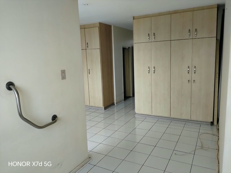 A spacious bedroom featuring extensive built-in wooden cupboards, tiled flooring, and a wall-mounted safety grab rail.
