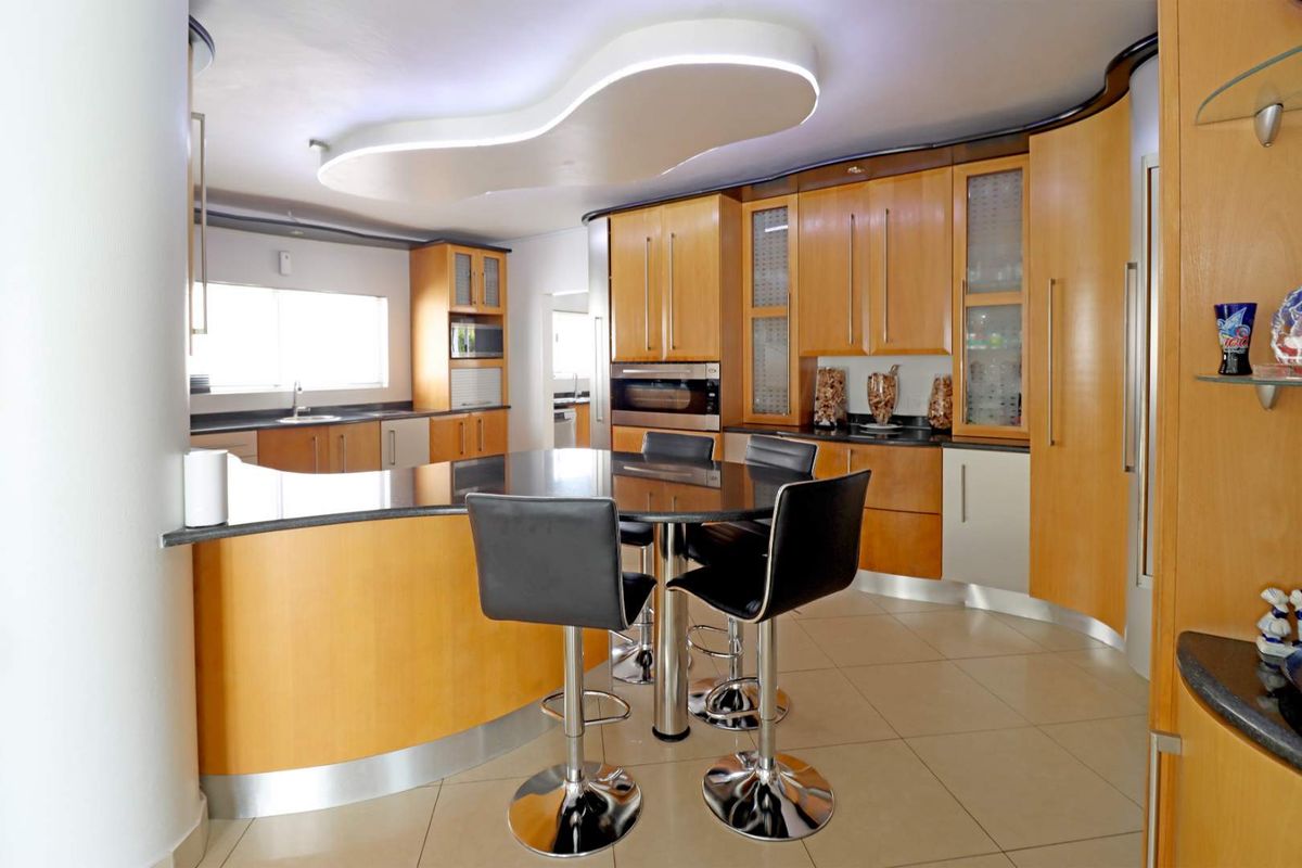 A spacious kitchen featuring curved wooden cabinetry, a dark stone breakfast bar, integrated oven, and a unique modern recessed ceiling light feature.