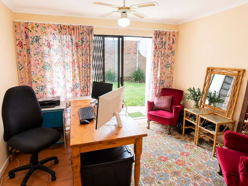 A functional home office space featuring tiled flooring, a ceiling fan, and direct access to the rear garden through a sliding glass door.