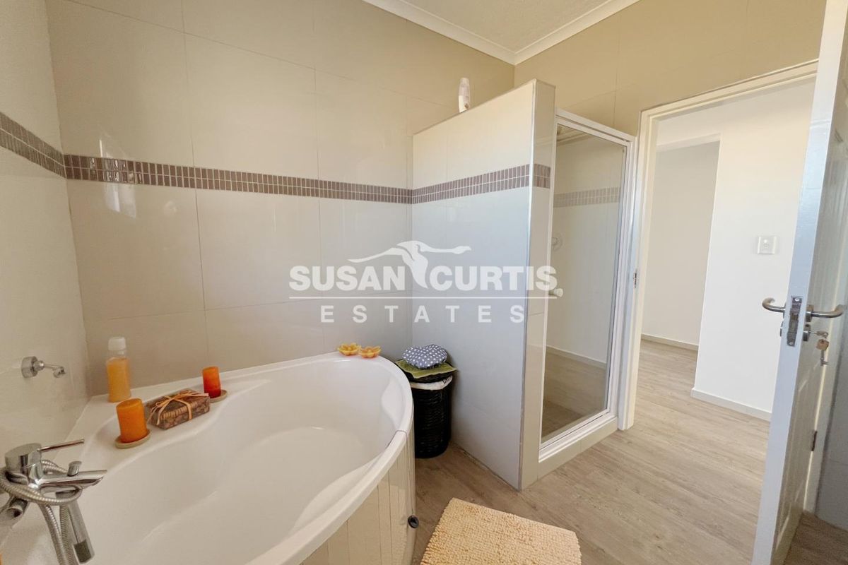 A well-maintained bathroom featuring a corner bathtub, a separate glass-enclosed shower, and neutral wall tiling with a decorative mosaic border.
