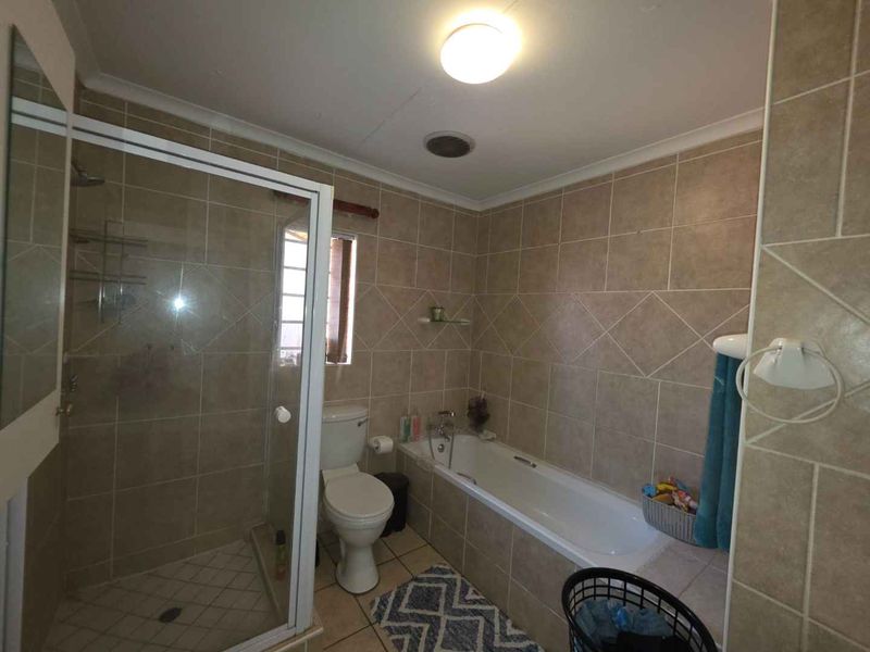 A functional bathroom featuring a shower enclosure, bathtub, toilet, and neutral wall and floor tiling.