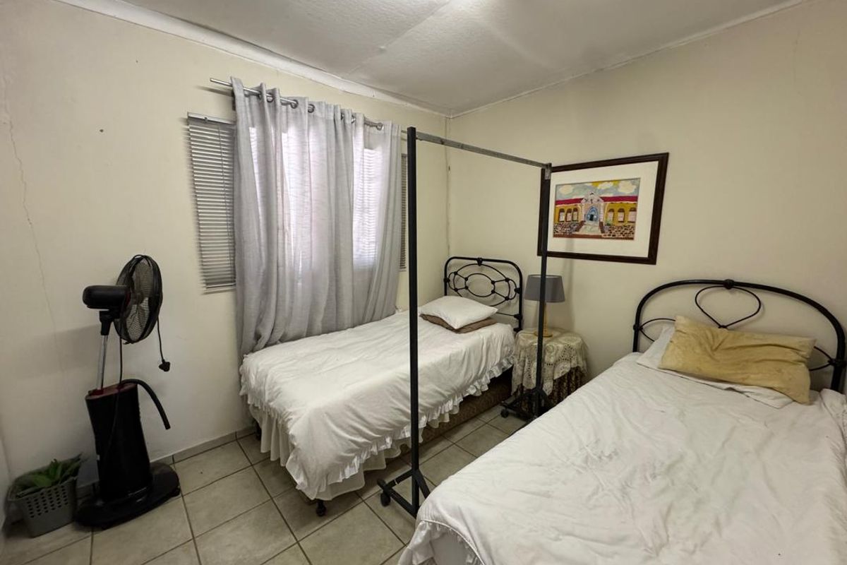 A bedroom featuring tiled flooring and a window with blinds, currently configured with two single beds.