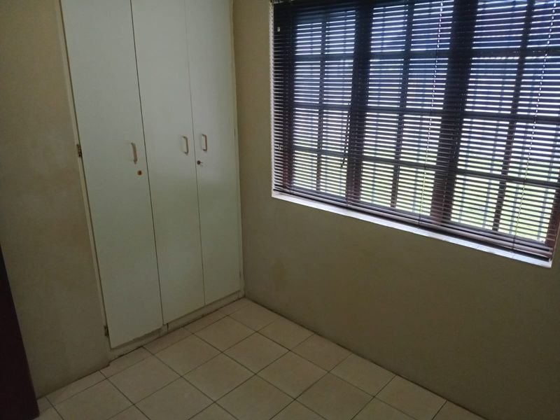 An empty bedroom featuring tiled flooring, built-in cupboards, and a window fitted with venetian blinds.