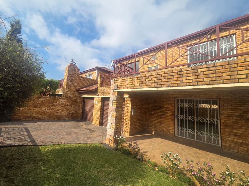 Front view of a face-brick townhouse featuring a double garage, paved driveway, and an upper-level balcony with metal railings.