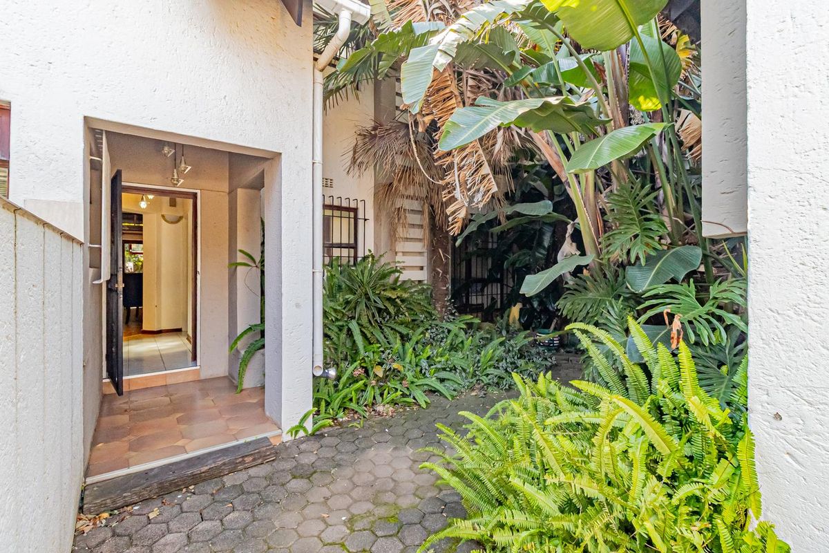 A private courtyard entrance featuring paved flooring and established garden beds, providing access to the main interior living space.