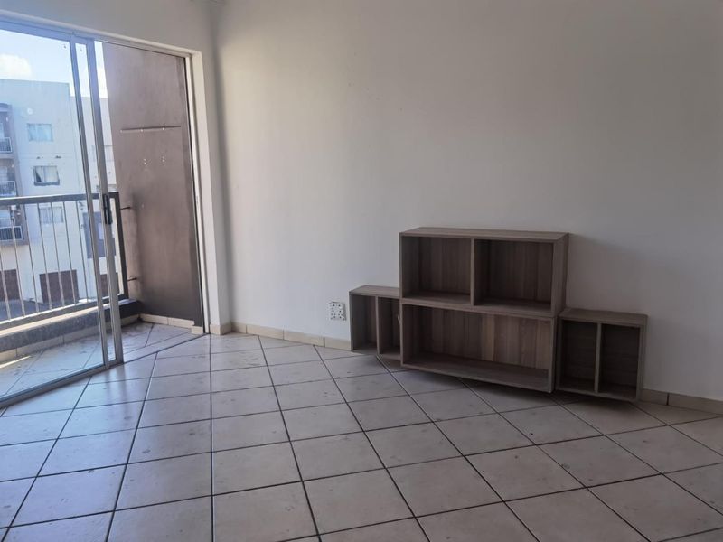 An empty living room featuring ceramic floor tiles and a sliding glass door leading to a balcony.