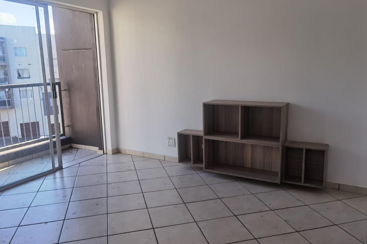 An empty living room featuring ceramic floor tiles and a sliding glass door leading to a balcony.