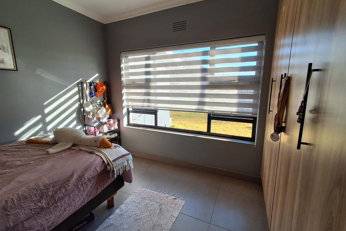 A well-maintained bedroom featuring modern tiled flooring, built-in wooden cupboards, and large windows with zebra blinds for adjustable natural light.