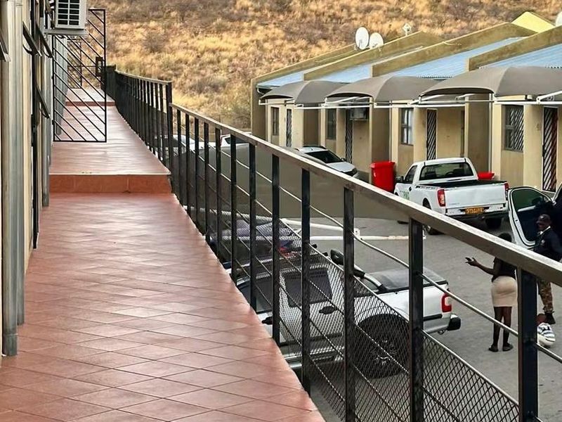 An elevated exterior balcony featuring tiled flooring and a metal safety balustrade, overlooking the apartment complex parking area.