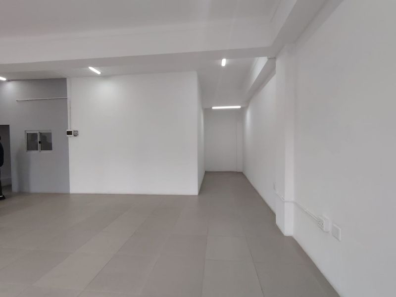A clean, vacant office space featuring neutral tiled flooring, bright recessed LED lighting, and a minimalist white interior finish.