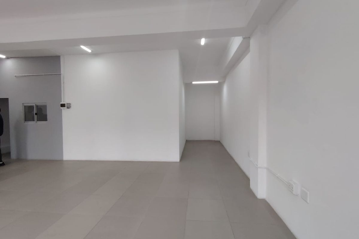 A clean, vacant office space featuring neutral tiled flooring, bright recessed LED lighting, and a minimalist white interior finish.