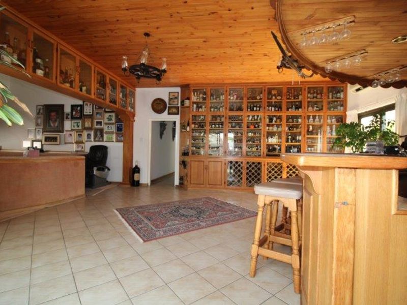 A dedicated bar area featuring extensive built-in wooden cabinetry, glass display shelving, a custom bar counter, and a warm timber-clad ceiling.