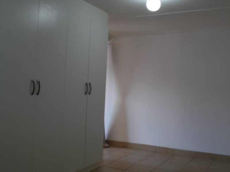 An empty bedroom featuring neutral tiled flooring and built-in white cupboards, providing a clean and functional space ready for personalization.