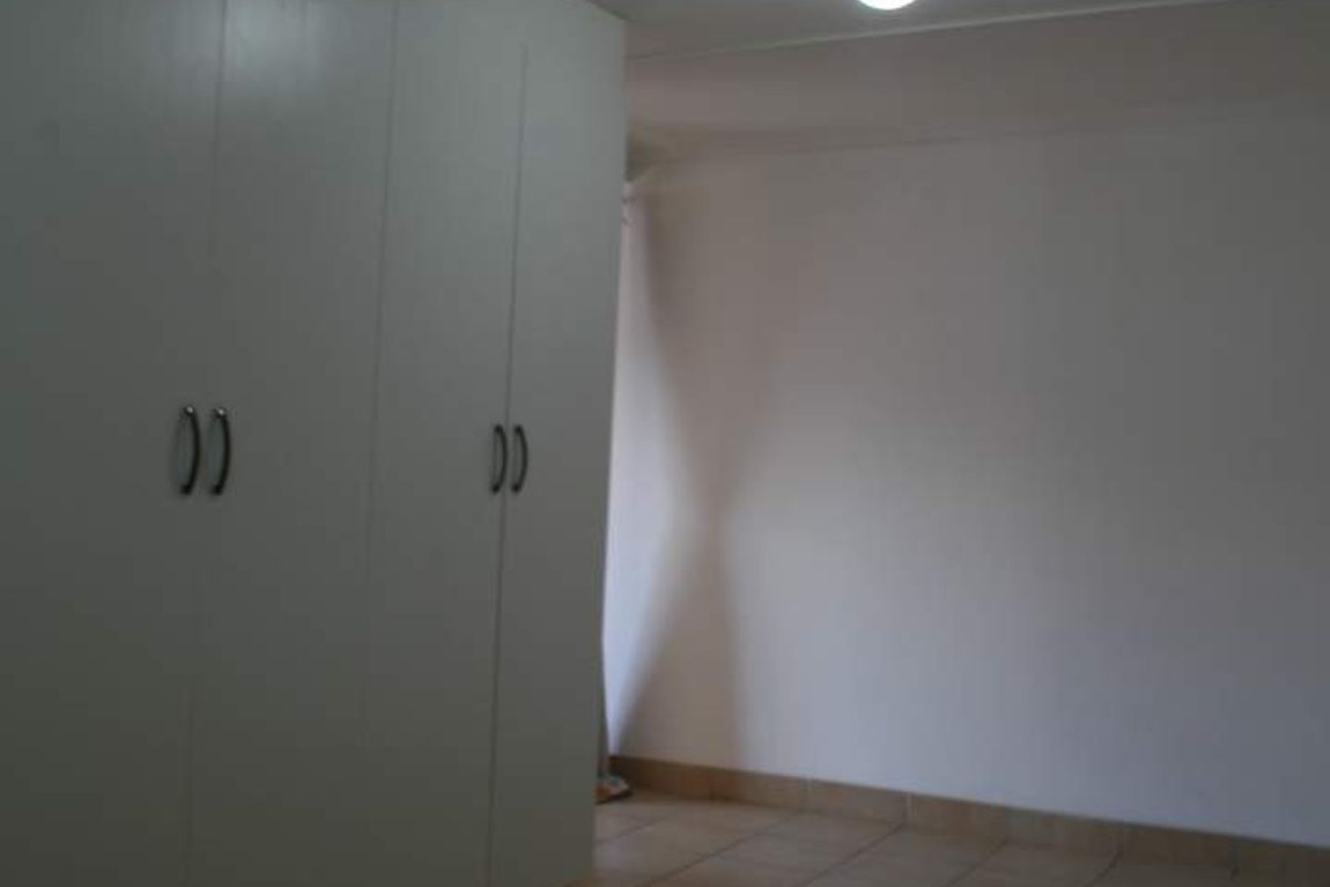 An empty bedroom featuring neutral tiled flooring and built-in white cupboards, providing a clean and functional space ready for personalization.