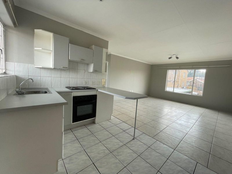 Spacious open-plan living area featuring a functional kitchen with built-in oven, hob, and breakfast bar, finished with neutral tiled flooring throughout.