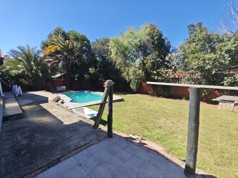 Rear garden area featuring a swimming pool, concrete patio space, and established lawn, enclosed by perimeter walls.