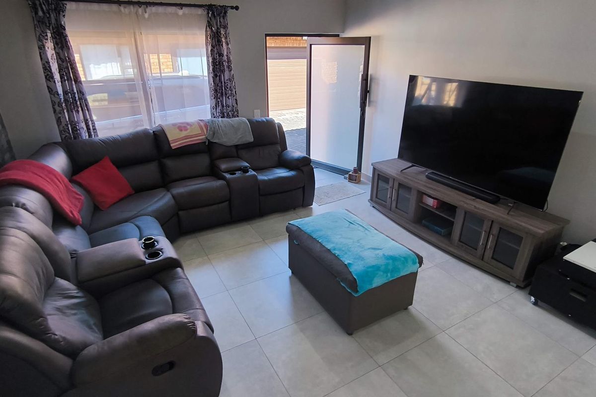 A comfortable living room featuring tiled flooring, a feature wall, and direct access to the exterior through a glass-panelled door.