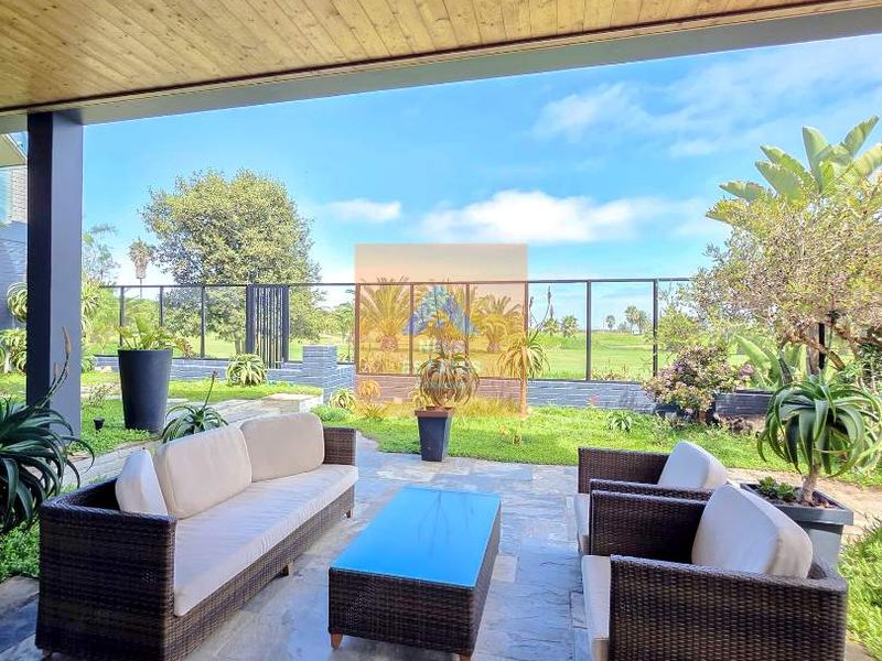 A covered patio featuring a timber-clad ceiling with recessed lighting and stone tile flooring, overlooking a landscaped garden and golf course view.