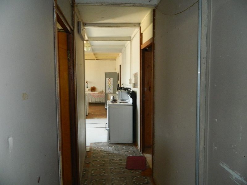 A narrow hallway leading into an open plan living and kitchen area, featuring dated finishes and exposed ceiling beams throughout.