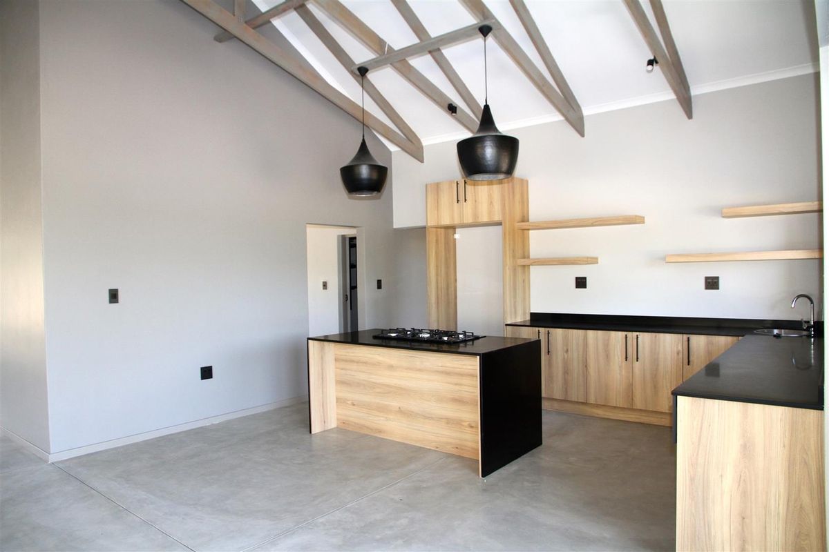 Modern open-plan kitchen featuring light wood cabinetry, black stone countertops, a central island with a built-in gas hob, and exposed timber ceiling beams.
