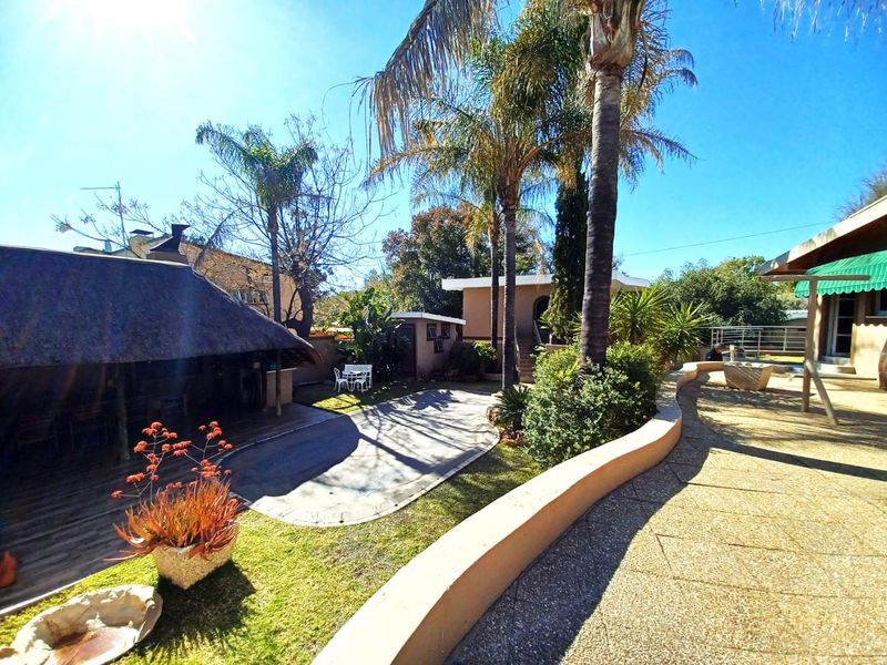 Spacious rear garden featuring a thatch roof lapa, paved patio areas, and established landscaping with mature palm trees.