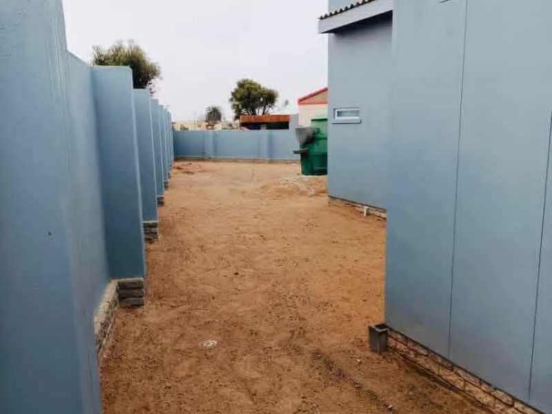 A side or rear exterior area featuring blue-clad walls and an unlandscaped, sandy ground surface.