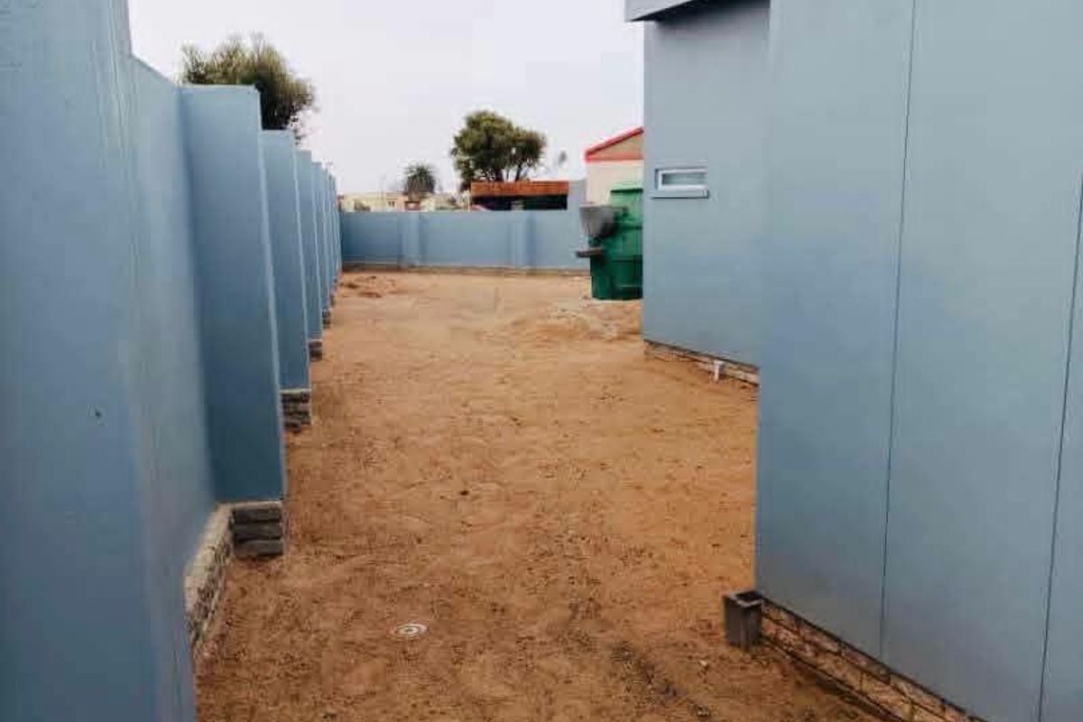 A side or rear exterior area featuring blue-clad walls and an unlandscaped, sandy ground surface.