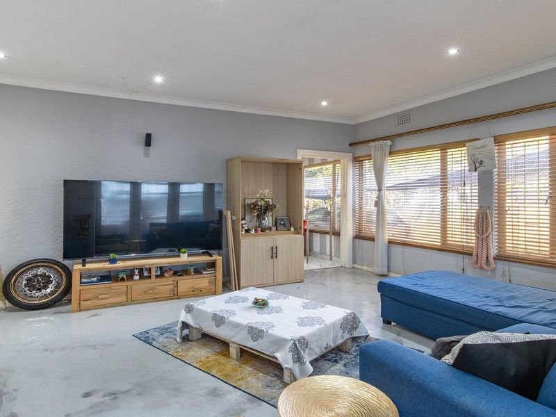 Spacious living room featuring polished concrete floors, recessed downlighting, and large windows fitted with venetian blinds.