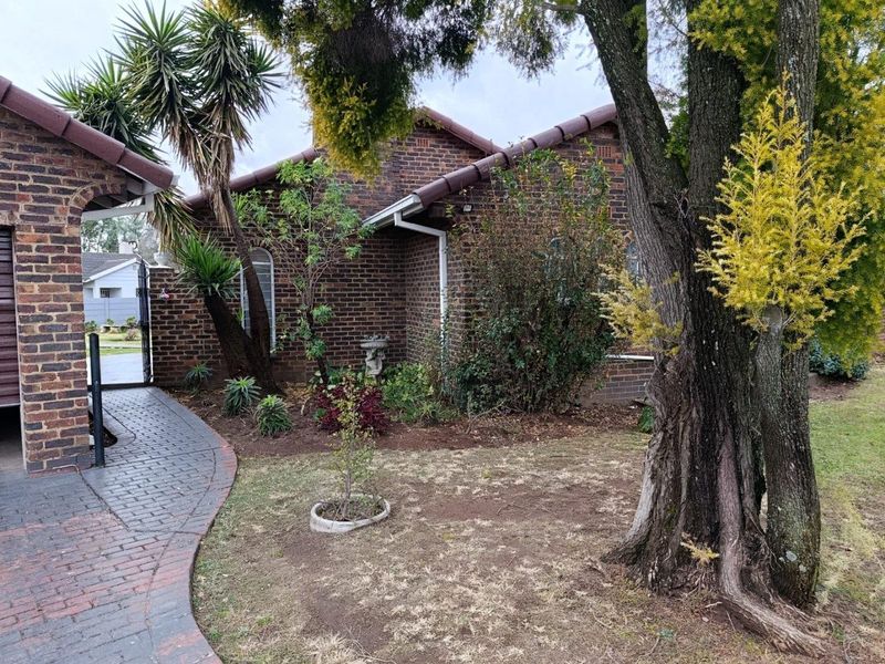 Front view of a face brick house featuring a tiled roof, paved walkway, and established garden area.