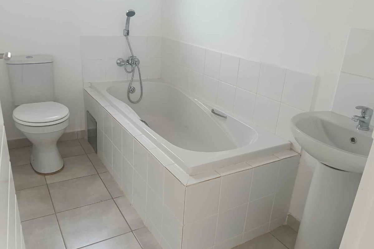 A functional bathroom featuring a white bathtub with shower attachment, a pedestal basin, and a standard toilet with tiled flooring.