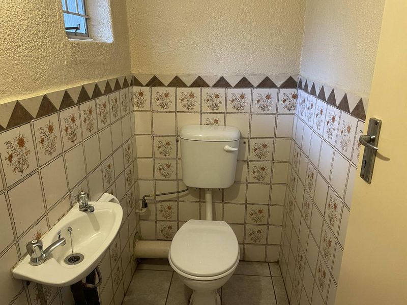 A compact guest bathroom featuring a toilet and wall-mounted basin with dated floral tile finishes.