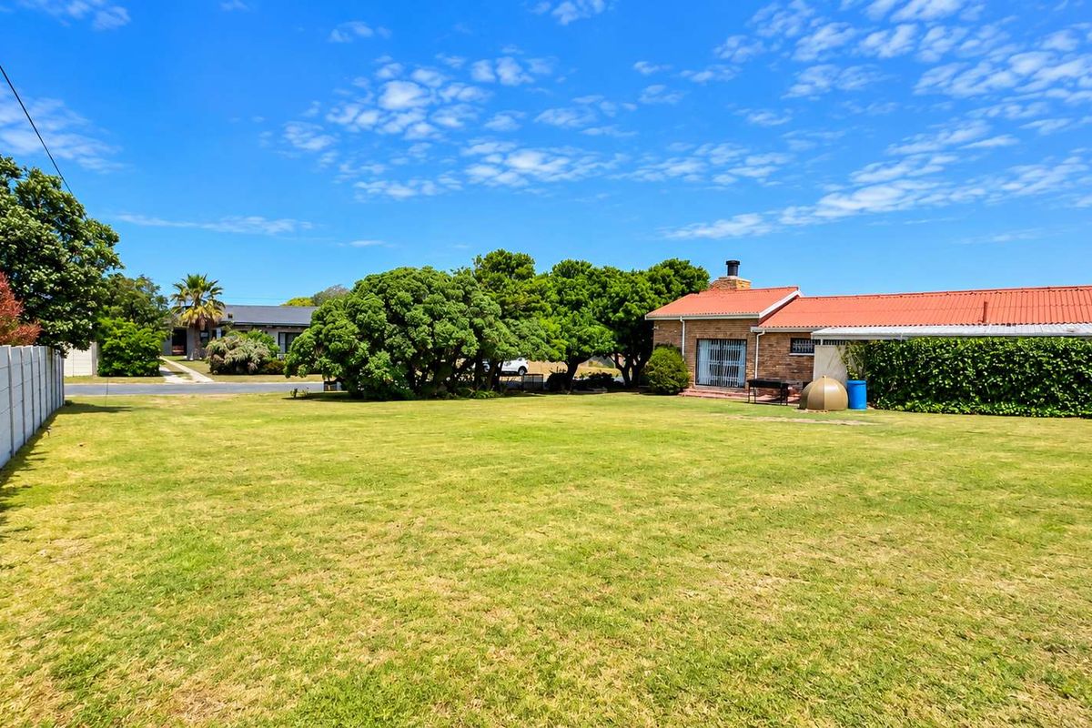 A spacious, well-maintained residential garden featuring a large lawn, mature trees, and a precast concrete boundary wall.